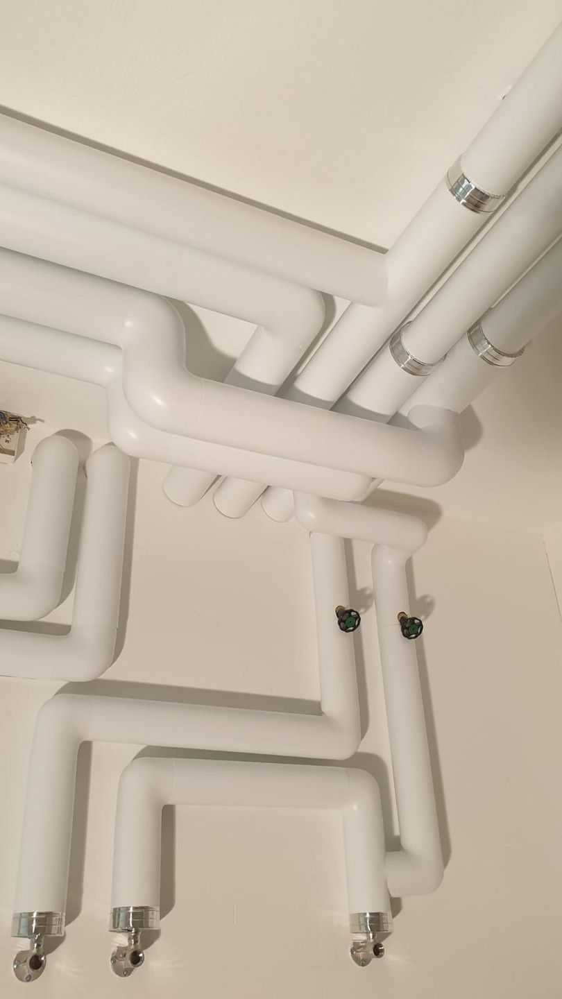 Sauber verlegte Sanitärleitungen mit weisser PVC-Ummantelung entlang einer Decke