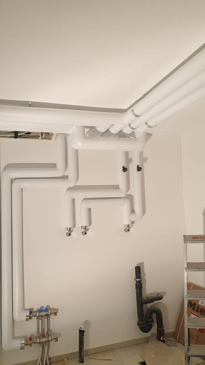 Weiss ummantelte Sanitärleitungen mit Anschlüssen entlang einer Wand